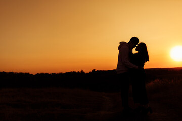 Silhouettes of lovely couple, handsome man gently hug beautiful woman at sunset, enjoy tender moments, caring husband and loving wife spend time together, weekends outdoors concept