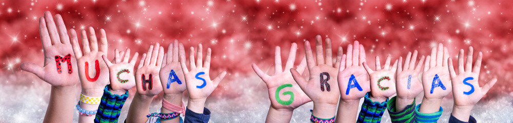 Children Hands Building Colorful Spanish Word Muchas Gracias Means Thank You. Red Snowy Christmas Winter Background With Snowflakes And Sparkling Lights
