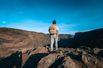 Fototapeta premium Adult tall man standing on top of cliff in summer mountains at sunny day and enjoying view of nature