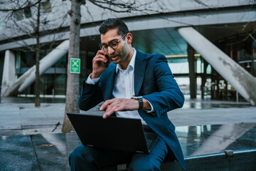 Mixed race businessman chatting on cellular device holding laptop while taking a break from work