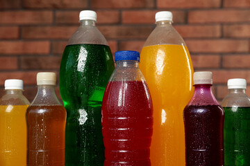 Obraz na płótnie Canvas Bottles of soft drinks with water drops near brick wall, closeup