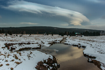 Winter view of mountain landscape, fresh cold stream and large meadow at Jizerka settlement,Czech republic. Winter nature in cloudy day.Peat bogs of Jizerka.Clear tranquil water snowy countryside.