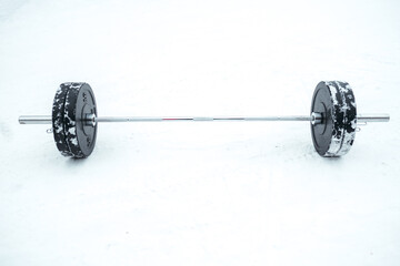The sports barbell for heavyweights lies in the snow, on the street. The barbell lies on the street for outdoor workouts
