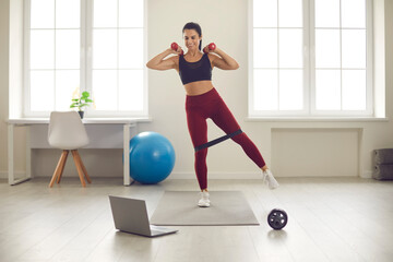 Woman training at home with hotels and rubber bands watching video guide with training on laptop.