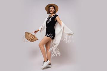 Full lenght studio photo of glad woman with short hairstyle in stylish boho summer outfit. straw hat and bag.