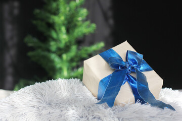 Gift with a blue bow on the background of the Christmas tree. Kraft paper packaging. Beautiful blue bow. A Christmas gift. New Year. Gift close-up