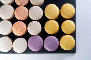 Macarons are laid out on a black slate in beautifully colored rows.