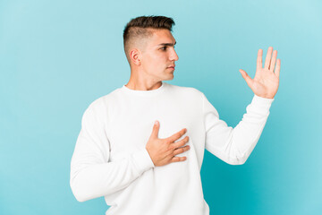 Young caucasian handsome man isolated taking an oath, putting hand on chest.