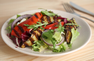 Delicious salad with roasted eggplant and arugula served on wooden table, closeup