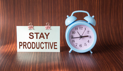 Stay productive, text on sticker and wooden background with blue alarm clock
