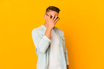 Fototapeta premium Young handsome caucasian man isolated blink at the camera through fingers, embarrassed covering face.