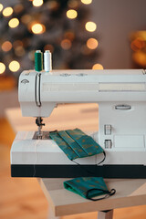 A close-up of sewing threads, sewing machine and handmade Christmas designed cotton face masks. Christmas DIY and handmade concept