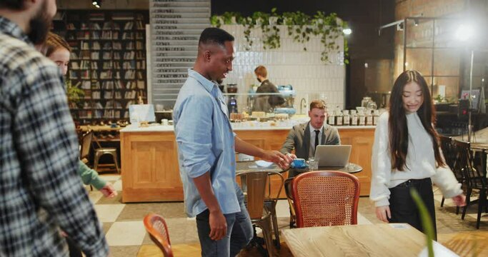 Young happy multi-ethnic people arriving to the modern cafe. Diverse beautiful love couples best friends communicating about lifestyle sharing table in coffeeshop.