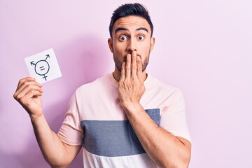 Young handsome man with beard asking for equality holding paper with transgender symbol covering...