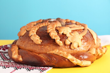 Rushnyk with korovai on yellow table against light blue background, closeup. Ukrainian bread and salt welcoming tradition