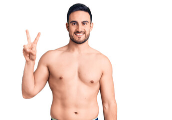 Fototapeta premium Young handsome man wearing swimwear smiling looking to the camera showing fingers doing victory sign. number two.