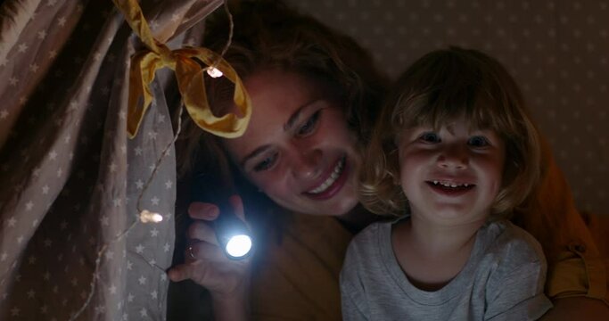 Positive caucasian woman spending time with her baby boy. Young mom is reading book of fairy tales for kid. Family in cozy tent in bedroom in evening 4k footage