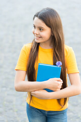 She has got the book she needs. Happy child hold book outdoors. Cute bookworm wear long hair in...