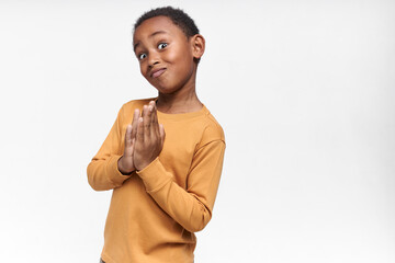 Body language. Handsome dark skinned little boy making funny grimace, keeping hands pressed...