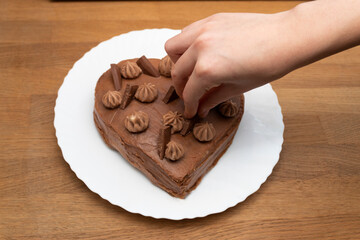 Woman decorates  heart-shaped cake base on a white plate. Wooden background.Selective focus.
