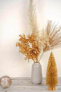 Composition of pampas grass with New year golden branch decoration in a vase on a white wall and wooden table background. Golden Fir tree near vase. Holidays decor concept. Hight quality photo