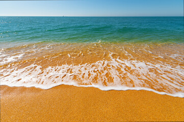 Soft wave of the sea on the sandy golden beach in the morning. Calm waves with foam on vacation and rest