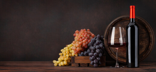Fototapeta na wymiar Wine bottle, grapes, glass of red wine and old barrel
