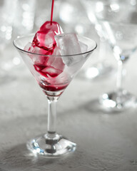 Black elder syrup is being poured on ice cubes in a glass