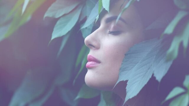 Beautiful fashion model woman enjoying nature, breathing fresh air in summer garden over Green leaves background. Harmony concept. Slow motion 4K UHD video.