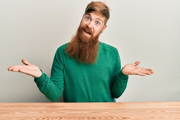 Young irish redhead man wearing casual clothes sitting on the table clueless and confused...