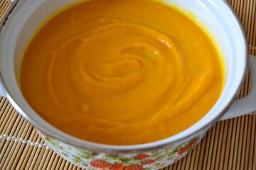 Pumpkin and carrot soup in white pot on wooden background