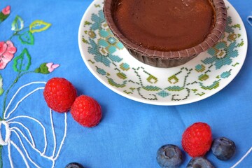 Close-up of a chocolate coulant on a porcelain plate on a table decorated with a blue tablecloth and in the background several more pieces of the porcelain set
