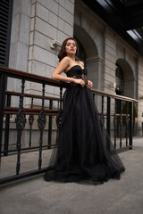 Full-length portrait of an elegant brunette woman with long hair in a black long evening dress.