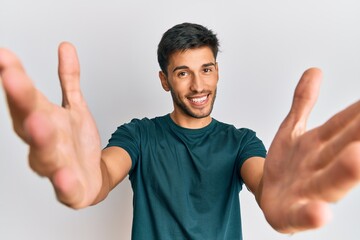 Young handsome man wearing casual clothes looking at the camera smiling with open arms for hug. cheerful expression embracing happiness.