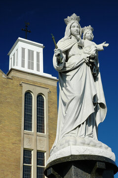 White Statue of Mary holding Jesus in front of Catholic church