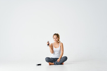 Obraz premium an athletic woman in a bright room sits on the floor and looks at dumbbells 