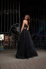 Obraz premium Full-length portrait of an elegant brunette woman with long hair in a black long evening dress.
