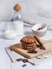 a stack of homemade chocolate cookies with chocolate chips, nuts and glass of milk  on a light table
