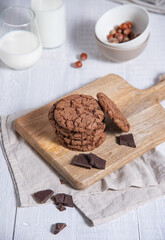 a stack of homemade chocolate cookies with chocolate chips, nuts and glass of milk  on a light wooden  table