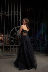 Full-length portrait of an elegant brunette woman with long hair in a black long evening dress.