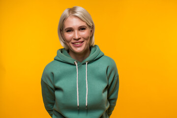 Smiling beautiful blonde in green hoodie looks to the camera on a yellow background. High quality