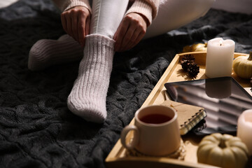 Woman in warm socks relaxing with cup of hot drink on knitted plaid, closeup