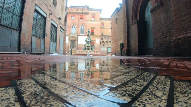 Slow motion Bologna in the morning, looking Neptune statue in main square with reflection in a puddle on the street