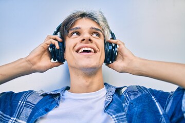 Young hispanic man smiling happy using headphones at the city.