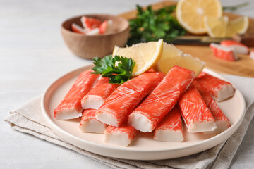 Plate of fresh crab sticks with lemon on white table, closeup