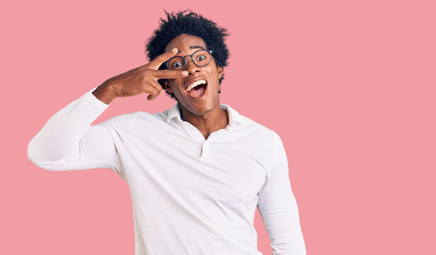 Handsome african american man with afro hair wearing casual clothes and glasses doing peace symbol with fingers over face, smiling cheerful showing victory