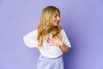 Young caucasian blonde woman laughing keeping hands on heart, concept of happiness.