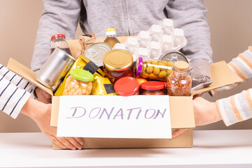 Volunteers hands holding food donations box with grocery products on white desk