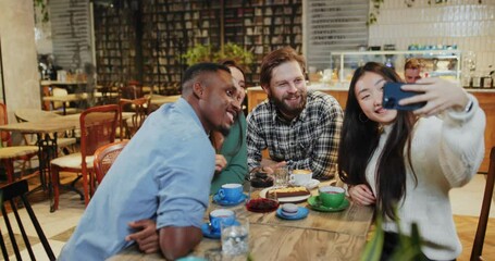 Mulit-ethnic attractive happy young people rejoicing hangout meeting in cafeteria taking selfie picture on smartphone smiling together. Friendship concept.