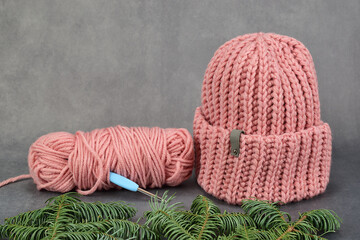 Fototapeta na wymiar Winter hat, knitted from thick pink yarn. Nearby there are the remains of the yarn, into which the crochet hook is stuck.